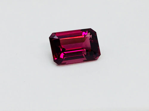 Medium size rectangular deep purple rhodolite garnet gem, on white background.