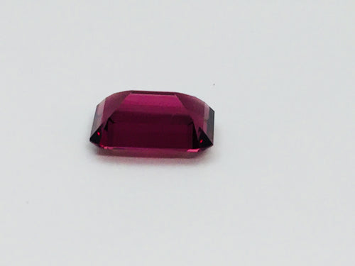 Medium size rectangular deep purple rhodolite garnet gem, on white background.