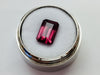 Medium size rectangular deep purple rhodolite garnet gem, on white background in gem jar.