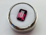 Medium size rectangular deep purple rhodolite garnet gem, on white background in gem jar.
