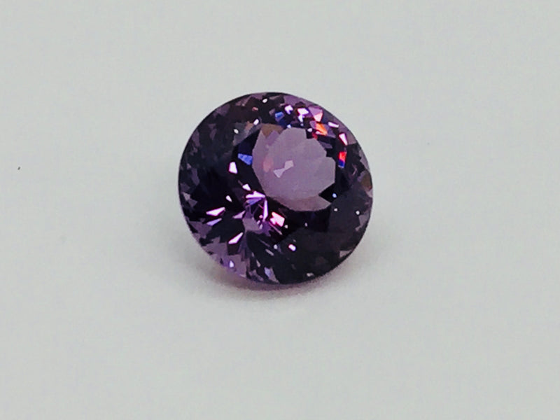Medium round deep purple spinel gem, on white background.