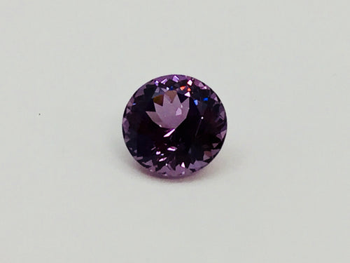 Medium round deep purple spinel gem, on white background.