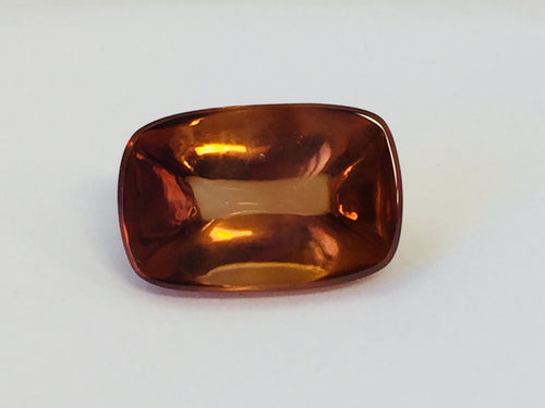 Rectangular deep golden brown cabochon zircon gem, on white background.