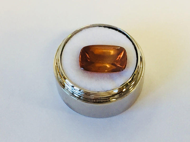 Rectangular deep golden brown cabochon zircon gem, on white background, in gem jar.