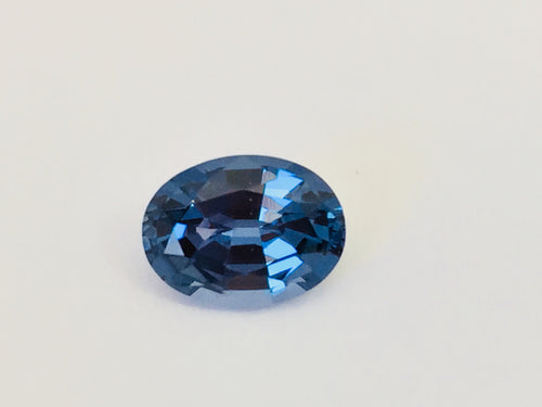 Small oval deep blue spinel gem, white background.