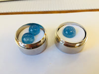 Three medium round medium blue cabochon aquamarine gems, white background, in gem jars.