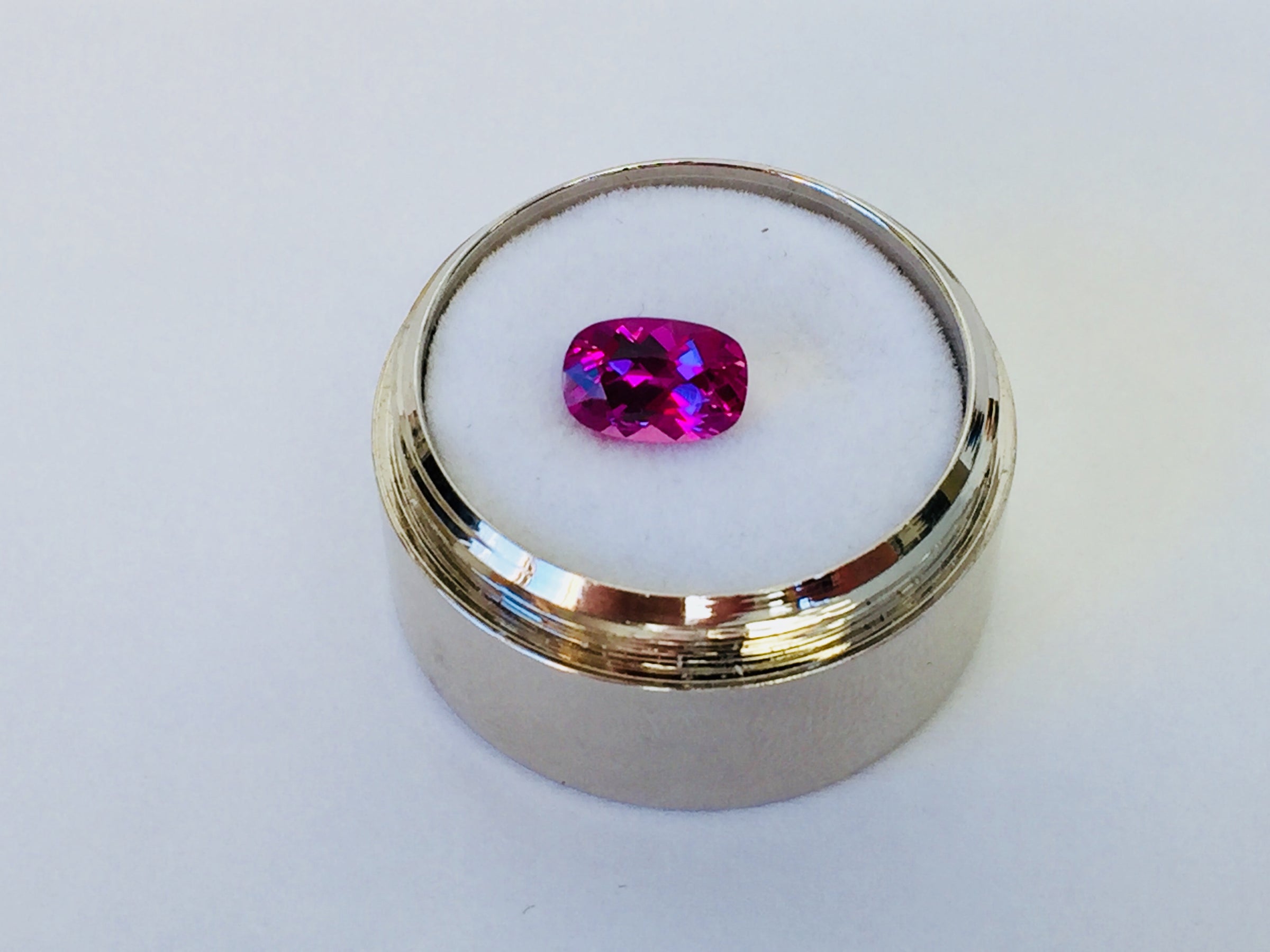 Small rectangle vivid pink sapphire gem, white background, in gem jar.