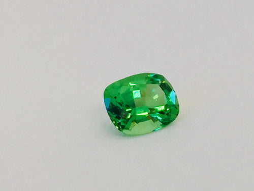 Small cushion shaped bright green tsavorite garnet gem, white background.