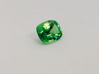 Small cushion shaped bright green tsavorite garnet gem, white background.