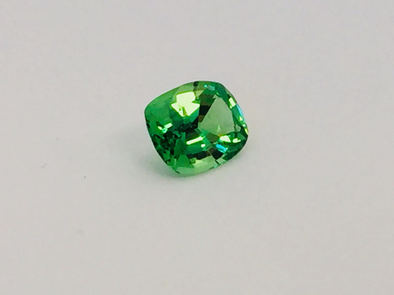 Small cushion shaped bright green tsavorite garnet gem, white background.