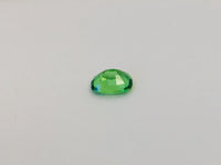 Small cushion shaped bright green tsavorite garnet gem, white background.