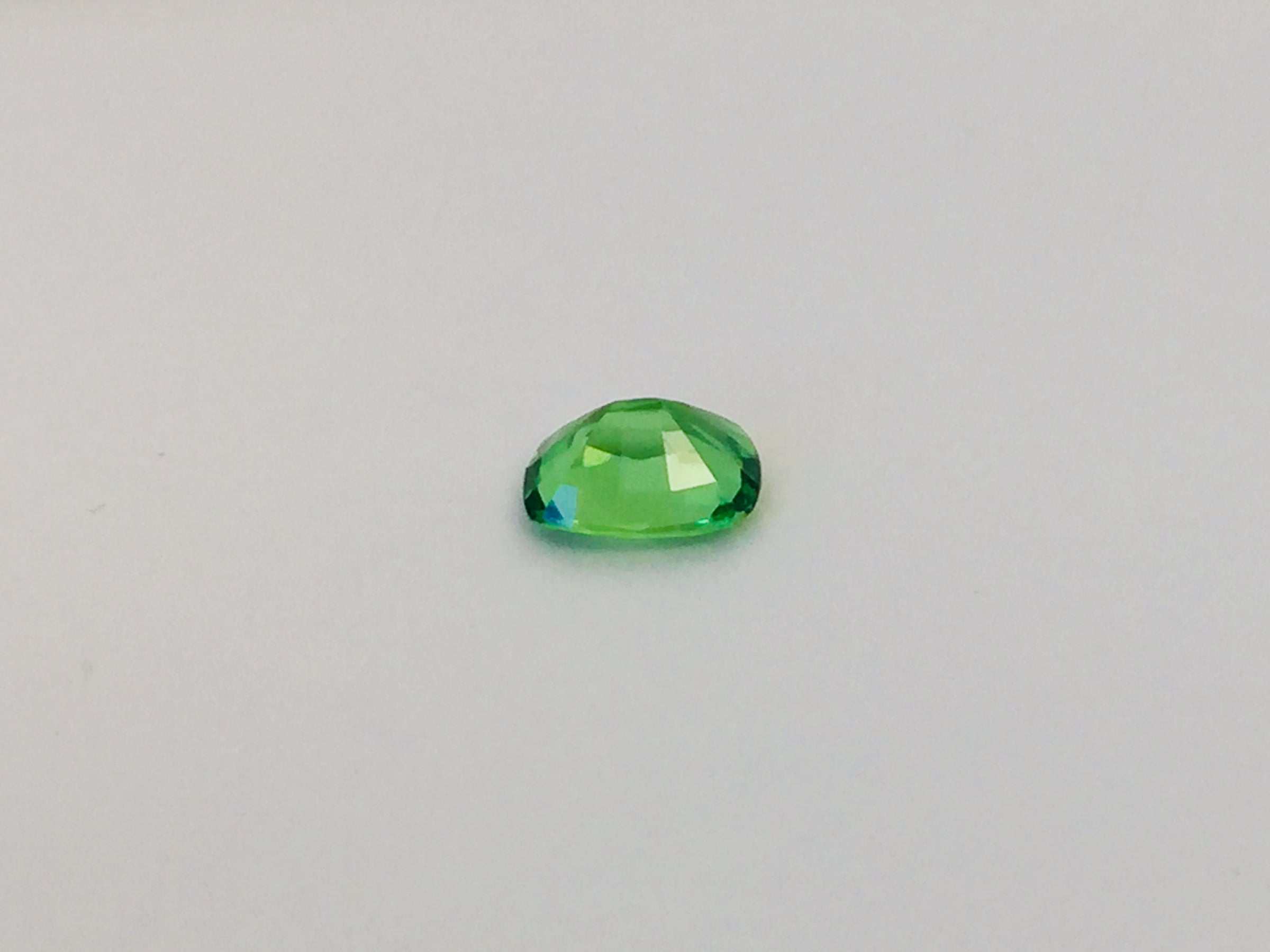 Small cushion shaped bright green tsavorite garnet gem, white background.