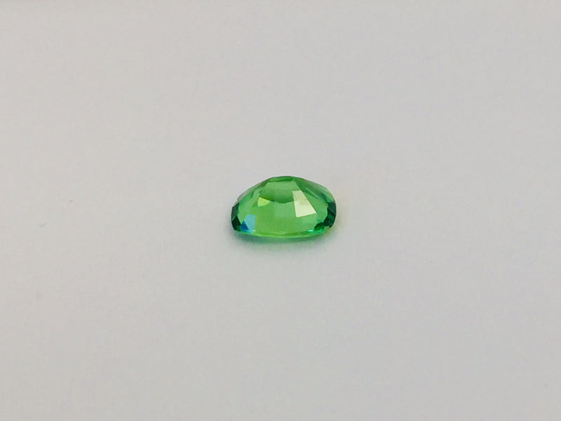 Small cushion shaped bright green tsavorite garnet gem, white background.