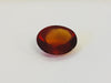 Medium oval deep orange red hessonite garnet gem, white background.