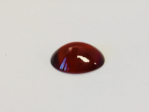 Medium oval deep orange red hessonite garnet gem, white background.