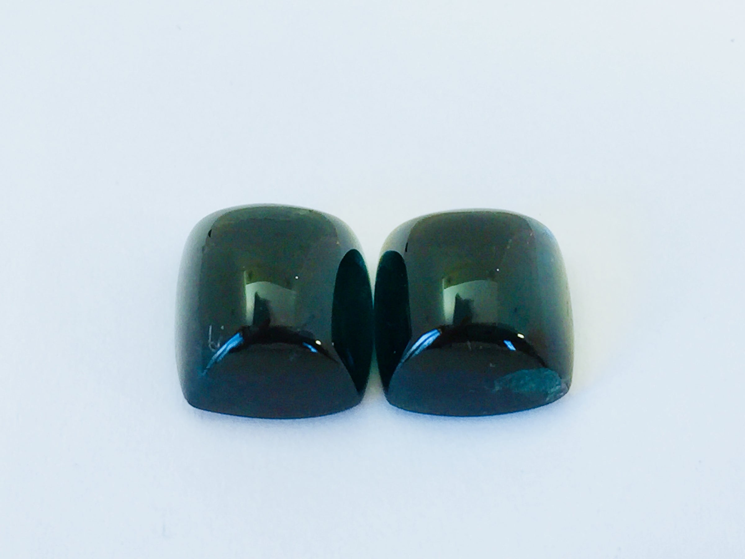 Pair of rectangular deep green blue indicolite tourmaline gems, white background.