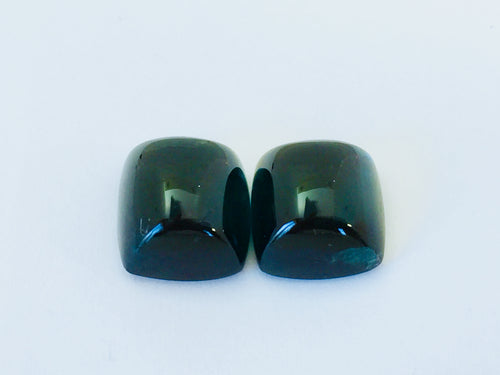 Pair of rectangular deep green blue indicolite tourmaline gems, white background.