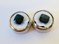 Pair of rectangular deep green blue indicolite tourmaline gems, white background in gem jars.