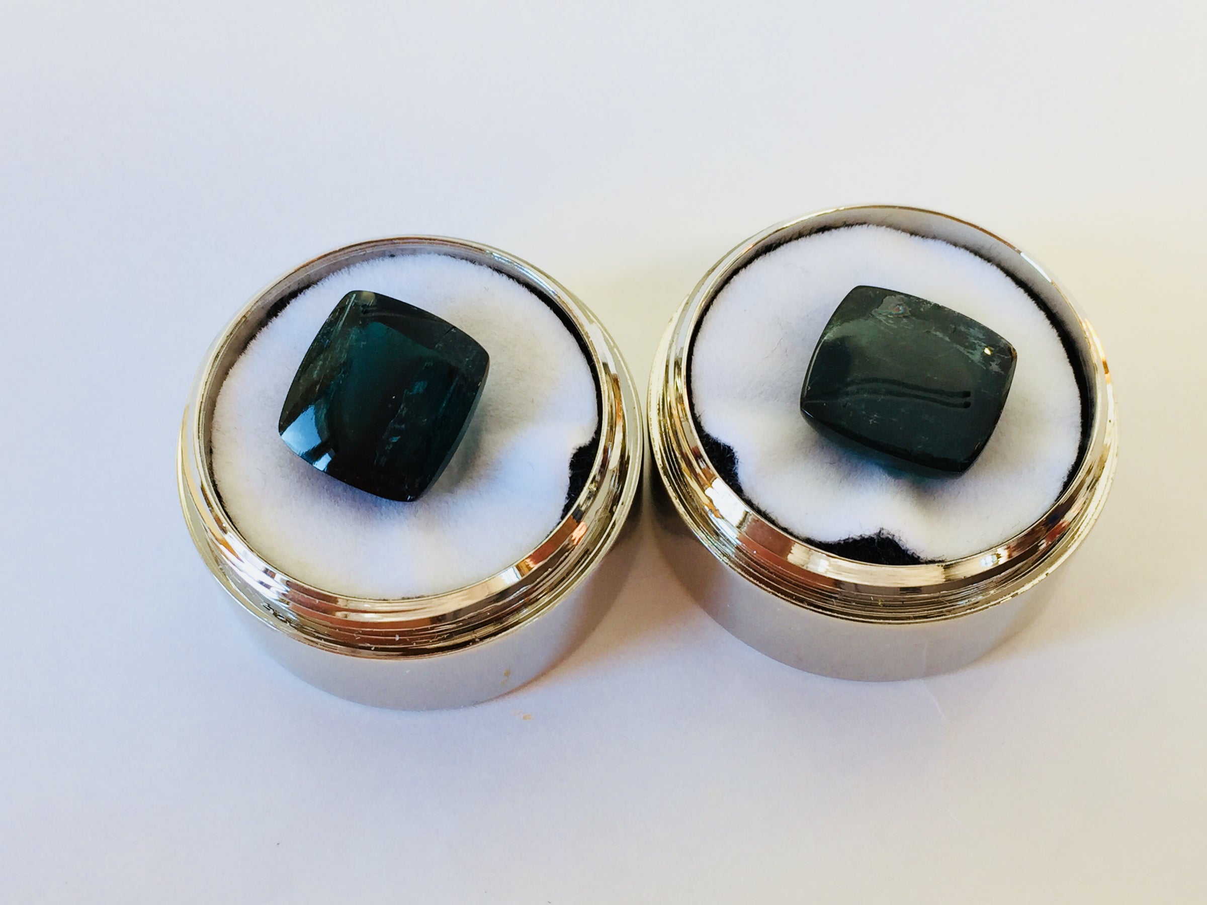 Pair of rectangular deep green blue indicolite tourmaline gems, white background in gem jars.