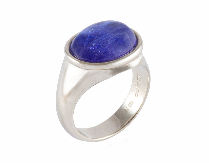 White gold ring set with medium oval cabochon of rich blue tanzanite. Gem is set in frame and lies across the finger. 