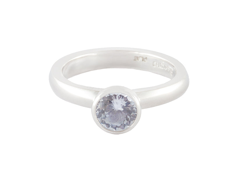 Platinum ring set with round pastel blue sapphire.  The gem is bezel or frame set and sits above the band.