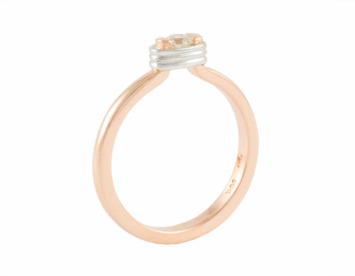 Thin rose gold ring set with a round diamond. Diamond setting is encircled by platinum wire, looks like it is lashed in.