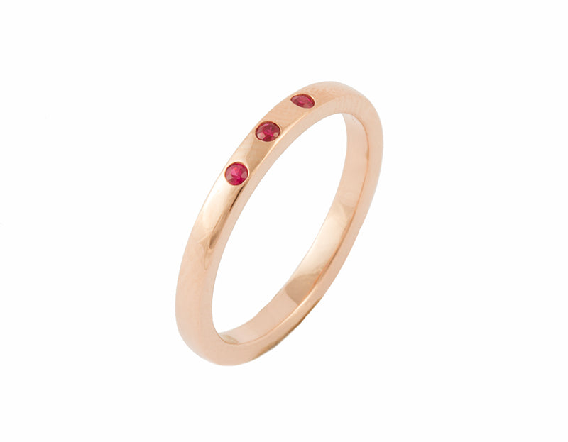 Thin rose gold band set with three bright red round rubies. The gems are set into the band.