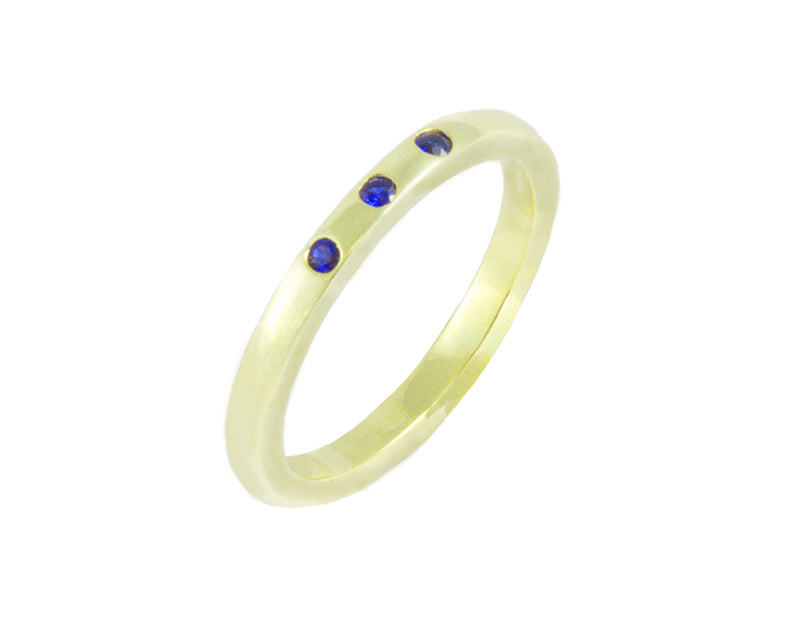Thin green gold band set with three bright blue round sapphires. The gems are set into the band.