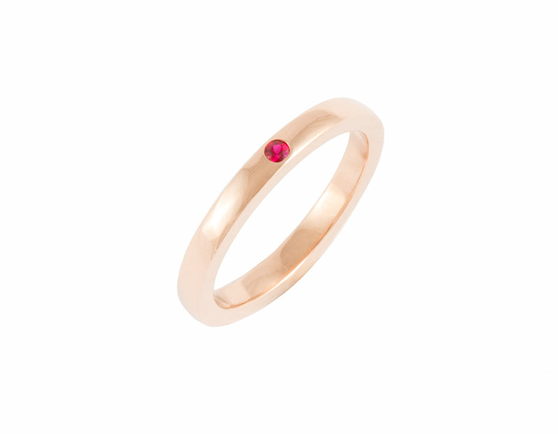 Thin rose gold band set with one bright red round ruby. The gems are set into the band.
