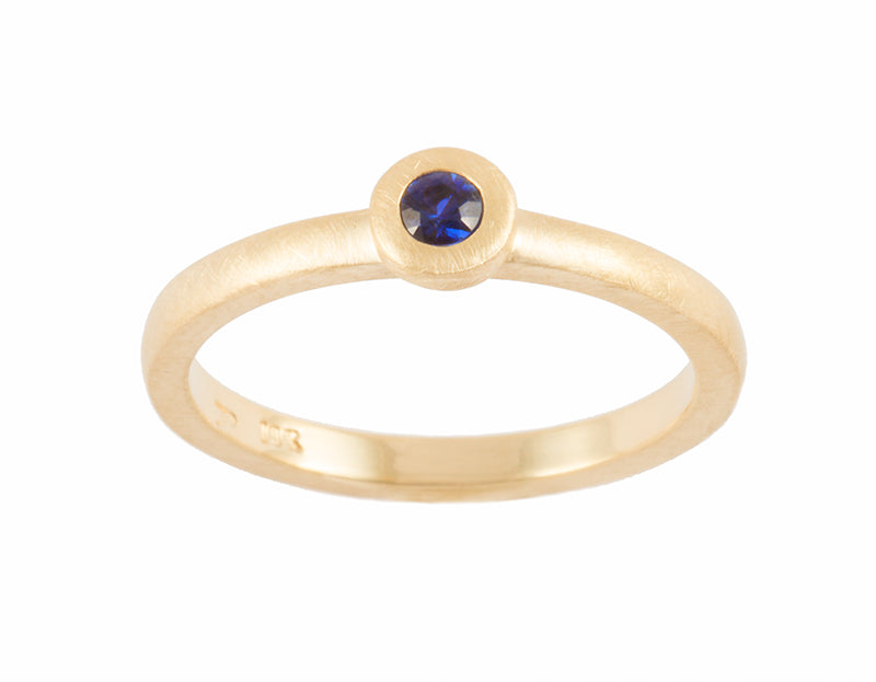 Thin 18 karat yellow gold band with soft matte finish set with bright blue round sapphire. Gem set in a frame that sits on the band.