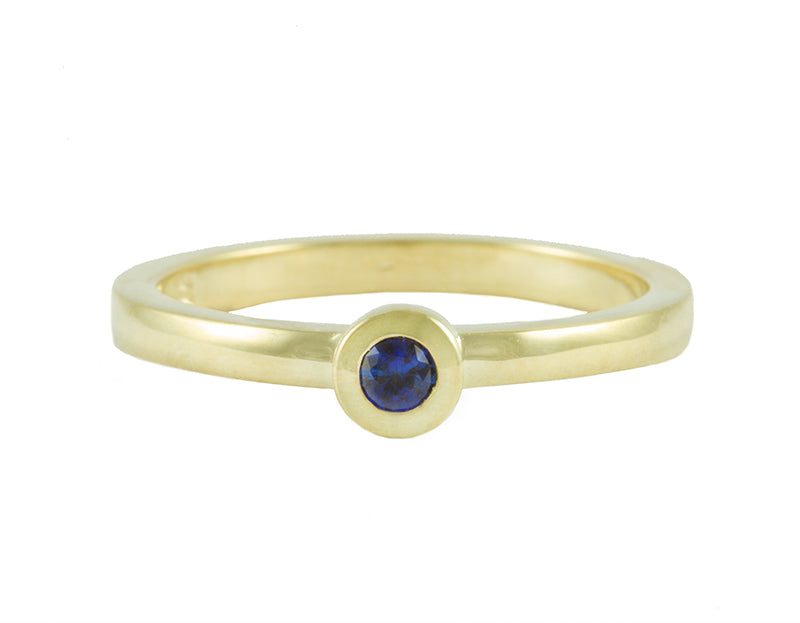 Thin 18 karat green gold band with soft matte finish set with bright blue round sapphire. Gem set in a frame that sits on the band.