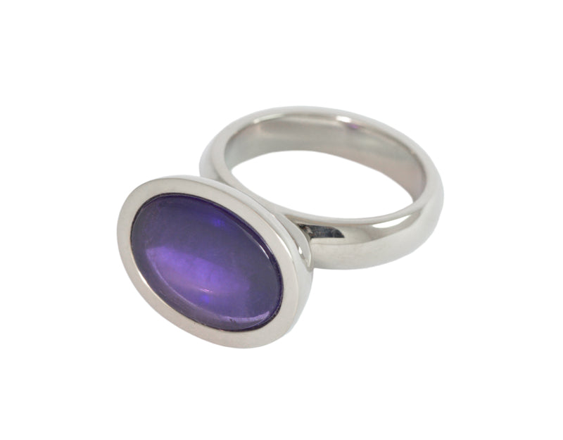 White gold ring set with upside down large oval cabochon of amethyst. Gem is set in a frame and lies across the finger..