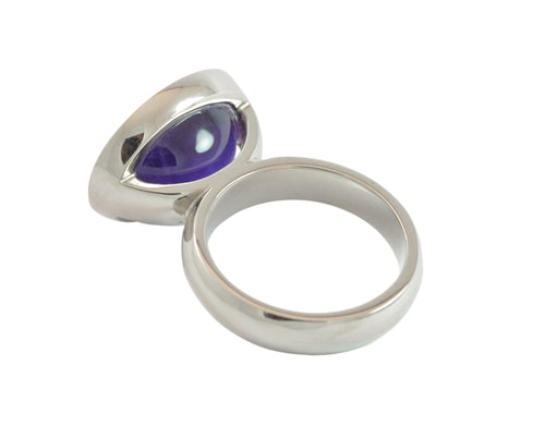 White gold ring set with upside down large oval cabochon of amethyst. Gem is set in a frame and lies across the finger..