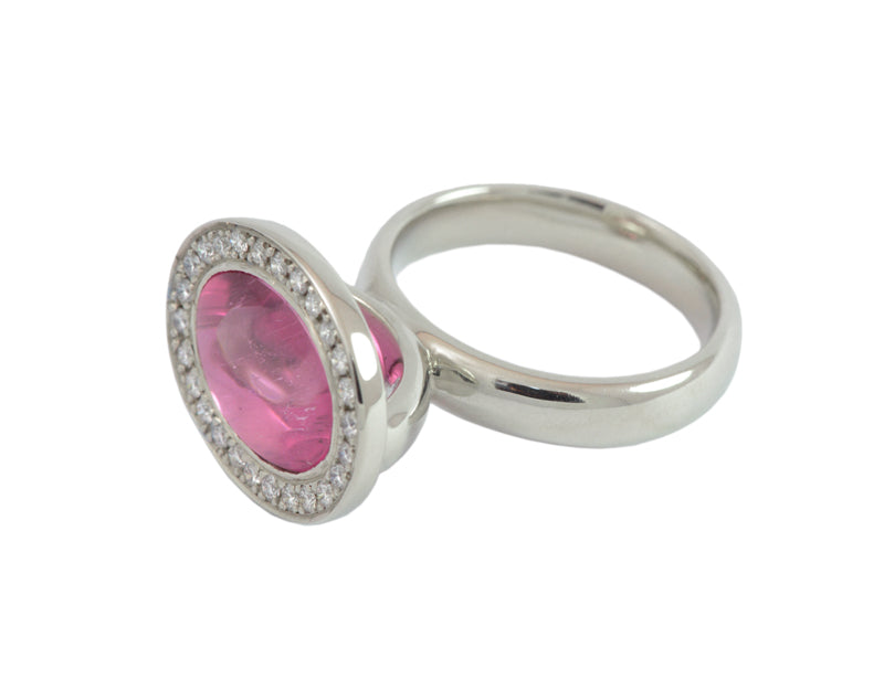 White gold ring with upside down cabochon of pink tourmaline. Set in frame and frame set with diamonds creating halo around tourmaline.