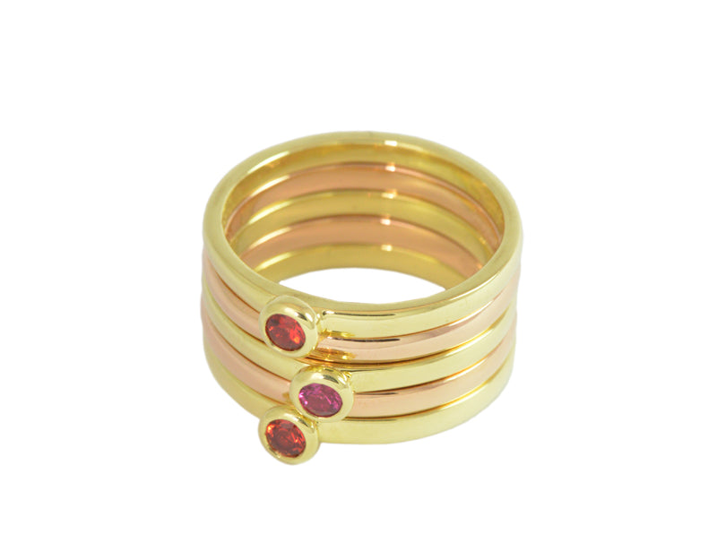 Stack of five thin rings, three of them with bright orange and pink sapphires, in green and rose gold.