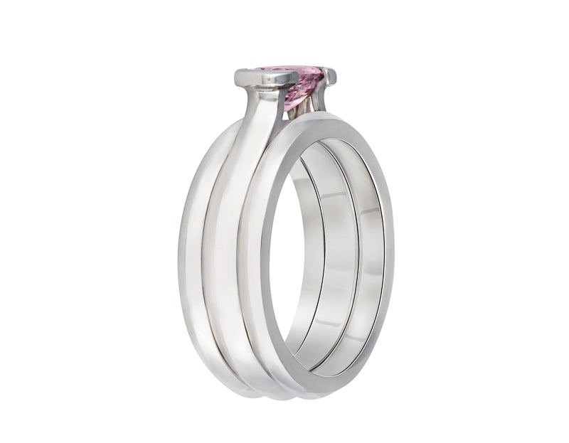 Platinum ring with natural pink sapphire, stacked with two matching platinum bands. The sapphire is oval and lies across the finger and is bezel set at two ends.