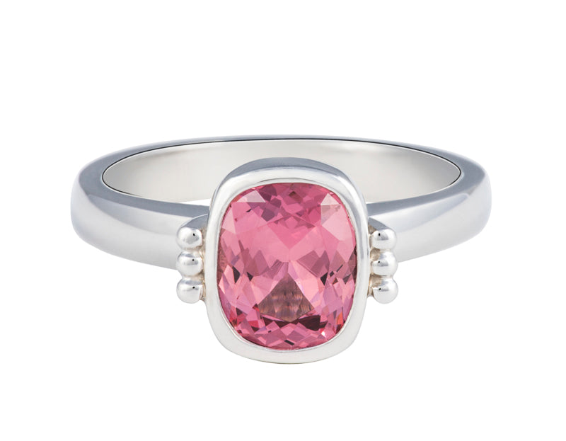 Platinum ring with natural pink spinel.  The gem is rectangular, lies parallel to finger, cut with a checkerboard pattern and surrounded by a frame, that is, bezel set.  Gem setting is raised above the ring.