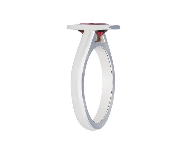 Platinum ring set with raspberry red rhodolite garnet in a frame, bezel. The gem is a thin rectangle lying parallel to the finger. Setting is raised above the band.