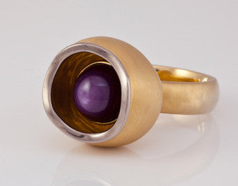 Red star sapphire set in bowl in yellow gold ring with white gold rim.