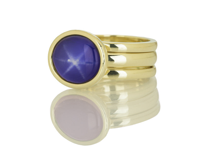 Blue star sapphire cabochon gem in green gold ring and matching green gold bands.
